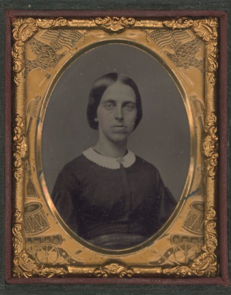 Ninth plate ferrotype/tintype waist-up portrait of an unidentified woman. She is wearing a dress with a white collar and a collar pin. Hand-coloring on the cheeks.