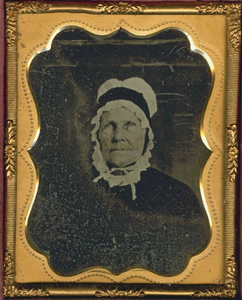 Ninth plate tintype/ferrotype. Quarter-length portrait of Rebecca Boone Grant Lamond. She is wearing a dark-colored dress, and a cap that ties under her chin and completely covers her hair. Hand-coloring on the cheeks. Mrs. Lamond was born June 4, 1774, married James Lamond on April 19, 1793, and died December 7, 1858. She was the niece of Col. Daniel Boone.