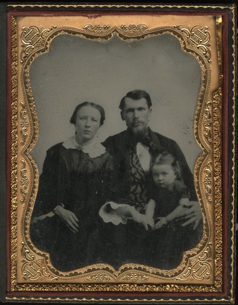 Half plate ambrotype of Franz Massing with his wife, and daughter Frances. Massing was the founder of the Madison Mannerchor in 1870. The family is seated. Both parents are holding the arms of their daughter who is sitting on Franz's lap. Hand-coloring on cheeks.