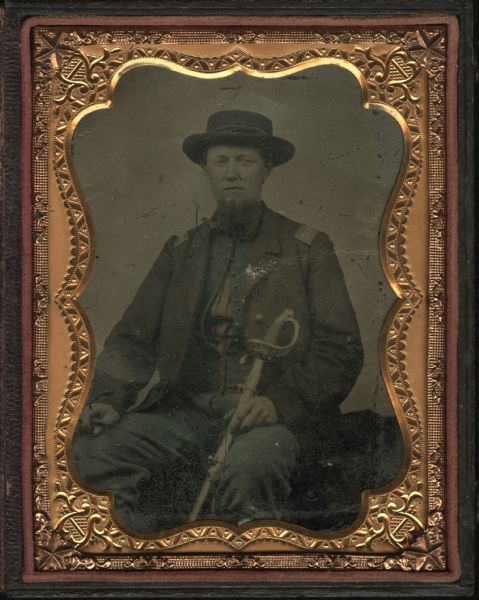 Quarter plate ferrotype/tintype of Lieutenant Albert Lamson, taken at Falmouth, Virginia. Lamson is posed, in military uniform, seated and holding a sword with one hand in his lap and holding a cigar in his other hand. Hand-coloring on his clothing.