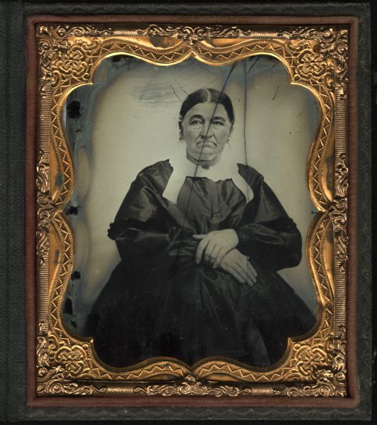 Sixth plate ambrotype portrait of Eleanor Nevins McCool. McCool is posed seated with her hands in her lap. She is wearing a dark dress with a white collar, and a white cap on her head.