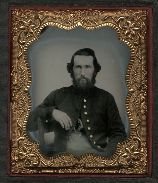Sixth plate tintype/ferrotype portrait of an unidentified soldier from the 13th Wisconsin Infantry. The man is seated with his arm draped over the back of a chair. The button at his collar is buttoned, but his coat is open. Hand-coloring on cheeks and gold details on buttons.