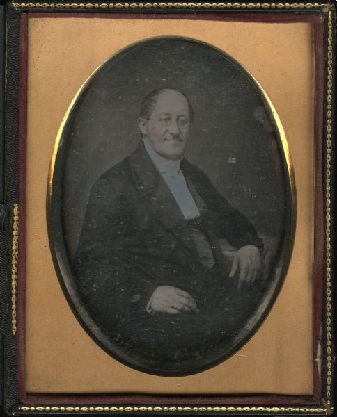Quarter plate daguerreotype of Reverend Nils Otto Tank, seated, facing front and to the right with left elbow on a table. 
Tank was a Moravian religious leader, land speculator, canal and railroad promoter, b. near Fredrikshald, Norway. The son of a wealthy politician and landowner, Tank was educated in various European universities. Disinherited after his first marriage and his conversion to the Moravian faith, Tank left Norway to become a teacher and missionary in the Dutch colony of Surinam. There he allegedly discovered rich gold fields, but soon left the colony, and in 1847 moved to Amsterdam, Holland. In 1850 he migrated to the U.S., and in New York became acquainted with a Milwaukee Moravian minister, A. Iverson. Intrigued by Iverson's story of the poverty of his parishioners in Wisconsin, Tank promised to help; he moved to Wisconsin, and purchased a tract of nearly 1,000 acres on the west bank of the Fox River at Fort Howard, where he planned to establish a communal society. He took up residence there in the Roi-Porlier-Tank cottage, but personal differences soon arose between Tank and Iverson over leadership of the community. The colonists themselves suspected Tank of planning to establish a tenant system or attempting to force them from their lands once improvements had been made. Their suspicions seemed to be confirmed when Tank refused to grant title to the land, and, aided by the governing body of the Moravian Church, they rejected Tank's leadership and left to establish a new settlement under Iverson. Shortly thereafter, Tank became associated with the Fox-Wisconsin River improvement scheme, but eventually lost heavily in the venture; he then turned his promotional activities to land speculations in Menasha and Manitowoc, and to railroad ventures, chiefly the Green Bay and Minnesota R.R. His wife, Caroline L.A. Tank, b. Amsterdam, Holland, lived on wealth inherited from her own family after the death of her husband. During the 1870's she gave money to several missions in China, to American schools, and to the city of Green Bay. In 1867 she donated a large collection of Dutch-language books to the State Historical Society, and at her death bequeathed the Tank collection of paintings to the Society.