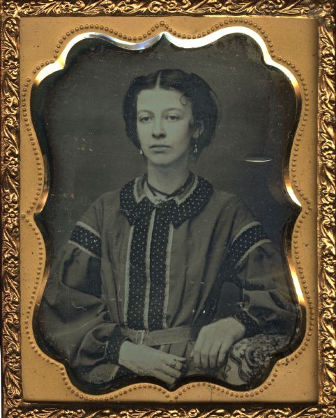 Ninth plate daguerreotype of Laura Smith. Miss. Smith was the sister of Rosellah Bowman; she died of consumption in Athol, MA. The portrait is a half figure showing the subject full face; her elbow is propped on a table and her hands are resting in her lap. She is wearing earring, a necklace, and a ring on her finger. Hand-coloring on cheeks.