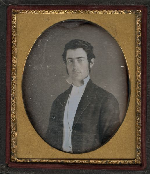 Sixth plate daguerreotype of Calvin Smith, son of Lyman Smith, and a cousin of Catherine A. Smith Hallock of Middleton, Wisconsin. Half figure, facing front and torso slightly turned to left, wearing unbuttoned coat and white shirt with stand collar, modest muttonchop sideburns, and slight mustache. Hand-coloring on cheeks. 