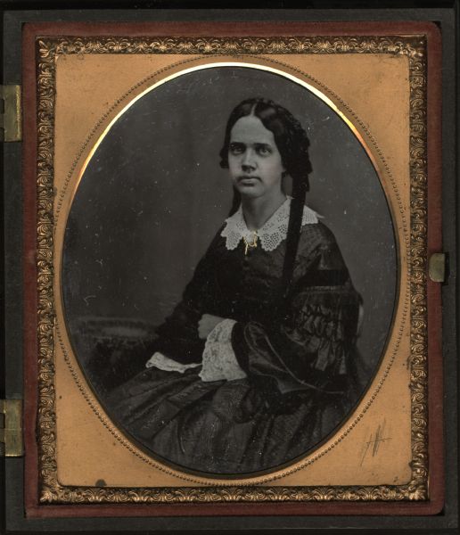 Sixth plate ambrotype of Mrs. William B. Noyes, first wife of William B. Noyes. Seated three-quarter figure facing front and slightly left, arms folded. She is wearing a lace collar with lace at cuffs of sleeves, two long hair ribbons, and a brooch at her neckline. Hand-coloring on cheeks and gold details on brooch. 