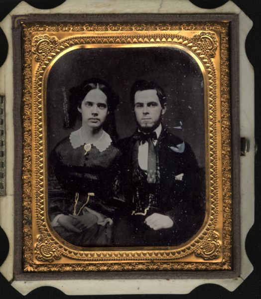 Sixth plate ambrotype of William B. Noyes and his first wife. Two seated half figures facing front. Noyes wears a bow tie with long tail, and his wife wears a white collar at her neck. Hand-coloring on cheeks. Gold details on brooch and the watch chains. They came from Brooklyn, New York to Janesville, Wisconsin. 