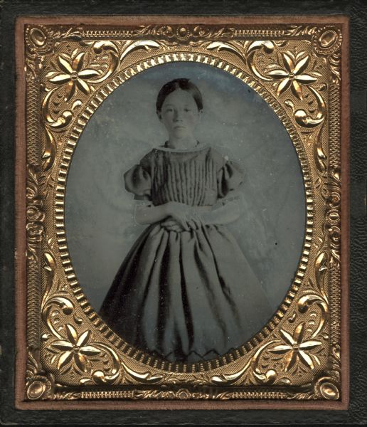 Sixth plate ferrotype/tintype of Josephine La Follette, sister of Robert (Bob) La Follette. Standing figure facing front, wearing dress with gathered bodice, short puffed sleeves and gathered skirt. Hand-coloring on cheeks. 