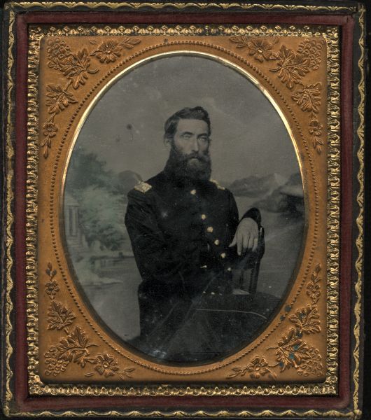 Sixth plate ferrotype/tintype of Captain Eri Sherman Oakley sitting in front of a painted backdrop. Seated three-quarter view of figure facing front but body turned to right, with left arm over chair back. Wearing Civil War Union uniform. Hand-coloring on cheeks and gold details on coat buttons, ring, and shoulder boards.