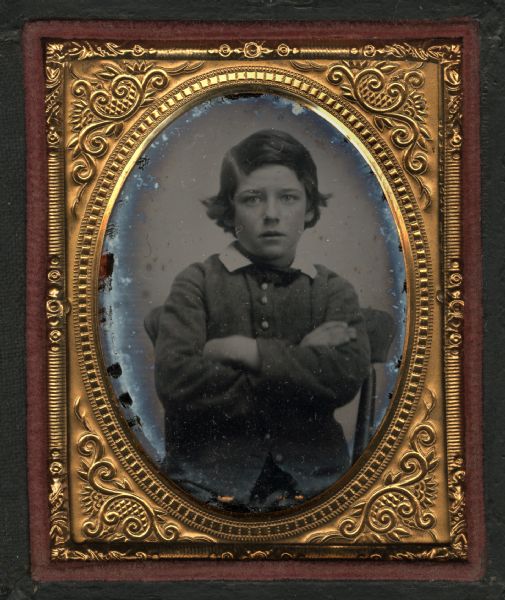 Ninth plate ambrotype of unidentified boy, probably the brother of G.W. Oakley. Seated half figure facing front, wearing buttoned jacket or sweater, white collar and tie, with arms folded.
