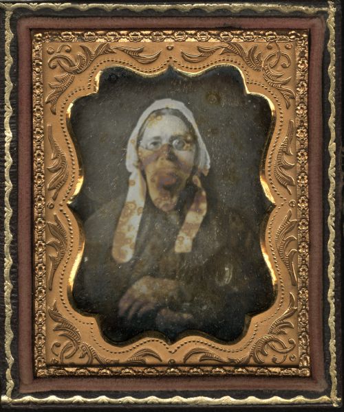 Ninth plate daguerreotype of a waist-up portrait of Susan Shriver Meyer Sweeney. Half figure facing directly front, wearing round-rimmed spectacles and white untied bonnet, with left hand folded over right.