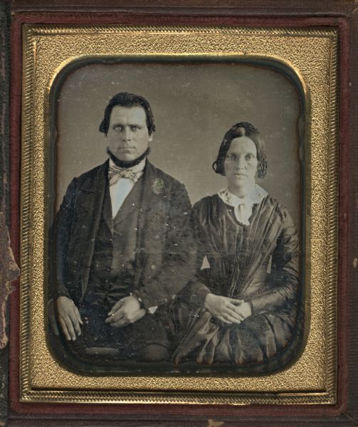 Sixth plate daguerreotype of Elbridge F. and Mary D. Ayer. Seated three-quarter figures, man on left, woman on right. Elbridge wears suit, vest and bow tie, and has a neck beard. Mary wears a long sleeve dress with lace collar with bow, and has her hands folded in her lap. Hand-coloring on cheeks. 