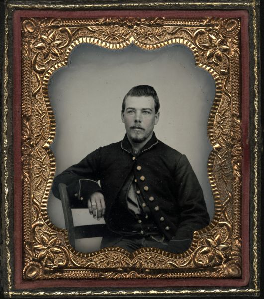 Sixth plate ferrotype/tintype of Henry Bowers. Seated half figure facing front with arm on chair back, wearing beard and moustache, and Civil War coat with only top button buttoned. Hand-coloring on cheeks and gold details on buttons. Subject has ring or bandage on fourth finger of hand. 