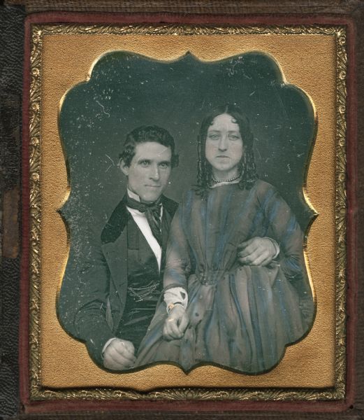 Sixth plate daguerreotype of L. Farr and E. Allen. The man is sitting and is wearing a suit, vest, necktie, and watch chain at his waist. The woman appears to be sitting on the arm of his chair, and is wearing a dress, pearl choker, and has ringlets framing her face. Hand-coloring on cheeks and on the woman's dress.