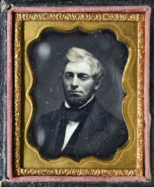 Ninth plate daguerreotype of unidentified man. Bust portrait, facing forward and torso slightly left. He wears a suit and cravat around a stand collar. Hand-coloring on cheeks. 