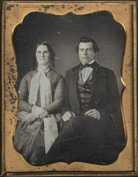 Full-length quarter plate daguerreotype of Sherman and Serepta Pratt. The Pratts moved from Bath, NY to Wisconsin Rapids, WI. They are seated facing forward. Serepta, on the left has her right arm crossed over her left on her lap. She is holding a small bag with chain handle; her hair is in long sausage curls, and a fabric scarf is pinned at her neck with the tails reaching below her knees. Sherman's left knee is crossed over his right, with his hands resting in his lap; he is wearing a three-piece suit and dark tie. 