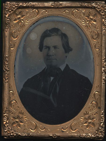 Quarter plate ambrotype of Jacob Spaulding. Quarter-length portrait, facing slightly left wearing coat with satin lapels, tie, and goatee. Cheeks hand-colored. 