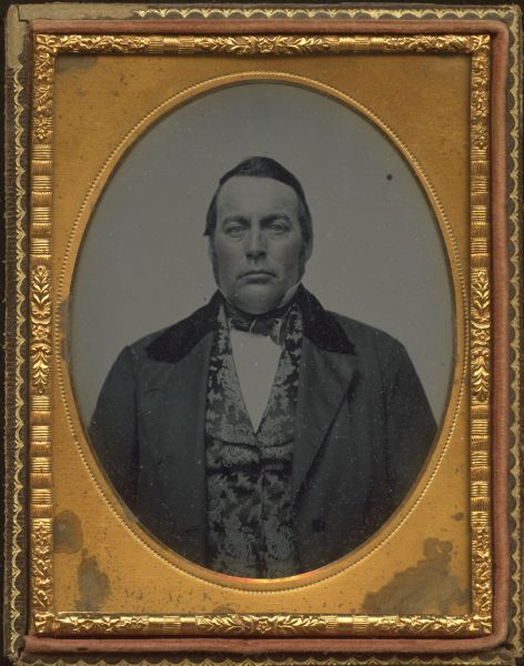Quarter plate ambrotype of an unidentified man, probably a relative of the Chandler family. Quarter-length portrait, facing front, wearing a suit coat with velvet collar, damask vest, and tie. Cheeks are hand-colored. 