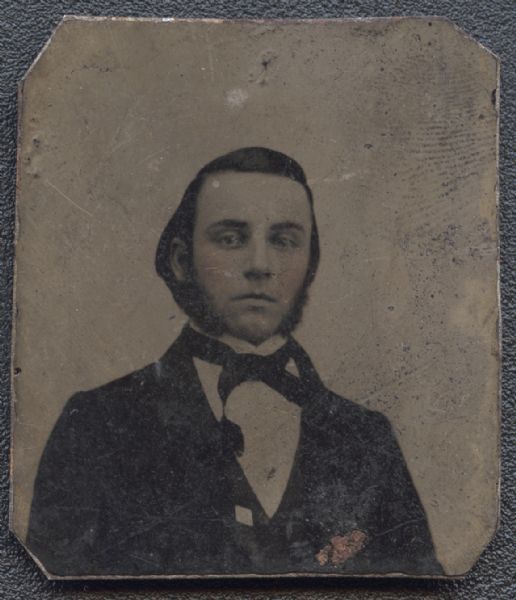 Sixteenth plate ferrotype/tintype of unidentified man. Quarter-length portrait, facing forward, wearing suit and tie, with sideburn whiskers. Cheeks are hand-colored. 