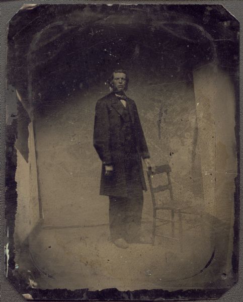 Ferrotype/tintype of Captain Peter Smith. Full-length portrait, facing front, with body facing slightly right, with his left hand on the back of a chair. He is wearing a knee-length coat, and has long sideburns.  