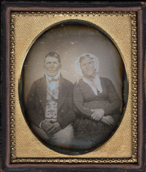 Sixth plate daguerreotype of Joseph Taylor and Constant Hoath Taylor, great-grandparents of Zona Gale Breese. They are seated, facing forward, with their hands folded in their laps. Joseph is wearing a suit, double-breasted plaid vest, and collar turned down over tie. Constant wears an empire-waist dress, white collar, and white bonnet tied under her chin. 