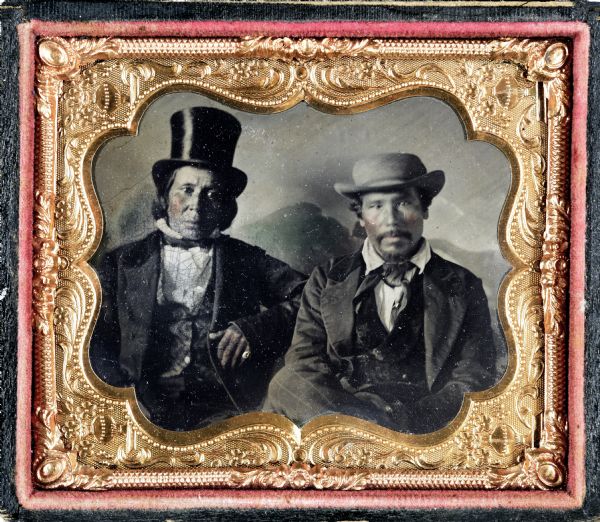 Sixth plate ferrotype/tintype of Menominee Indian chief Aquanama and Menominee Indian Paul Ackenebowa, seated, facing front, both wearing hats, coats and neck ties. Hand-coloring on cheeks and lips. Aquanama was a Menominee Indian chief.