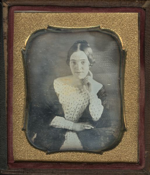 Sixth plate daguerreotype of Ann Elizabeth Stone, daughter of Samuel and Caroline Allcott Stone, taken in the mid-1840s. Three-quarter length seated pose, facing forward, with left elbow and right hand on cloth covered table, left hand on chin. She is wearing a printed dress, dark shawl, a brooch at the neckline, and a ring on right hand.
