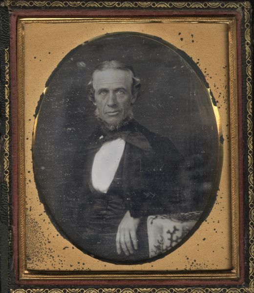 Sixth plate daguerreotype of Colonel Samuel Stone. Half length, seated, portrait, facing forward with left forearm on cloth covered table. He is wearing a suit, neck tie, and chin whiskers. 