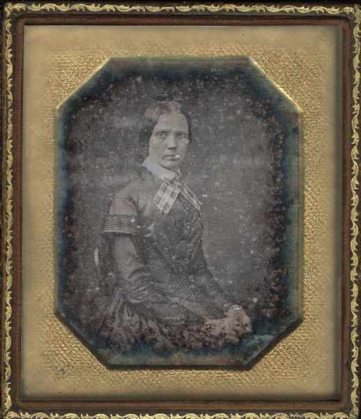 Sixth plate daguerreotype of Mrs. Thomas Stewart. Seated three-quarter figure, body facing right (proper left) and head facing front, hands in her lap. She wears a fan-front dark dress with large striped neck ribbon under a lace collar. 