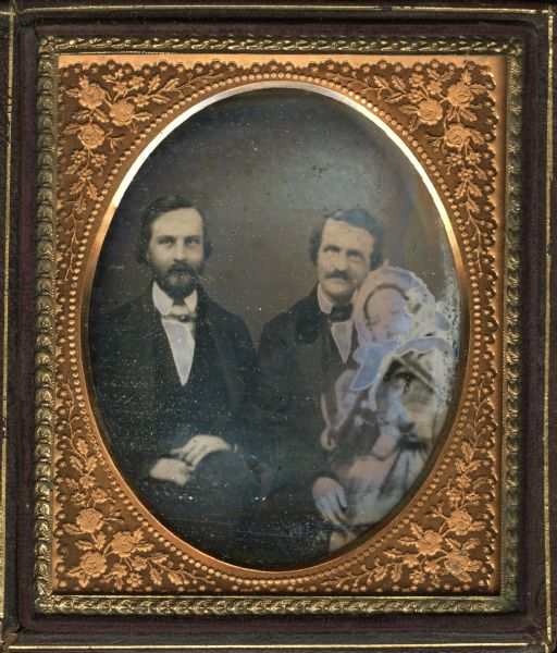 Sixth plate daguerreotype of Elisha Burdick with unidentified man and child. Men are seated, facing forward, wearing suits. Burdick on left, wears full beard and mustache, and has his hands in his lap. Hand-coloring on cheeks. Man on right has velvet jacket collar and wears a mustache. He is holding the child, who is wearing a plaid dress or coat and bonnet.