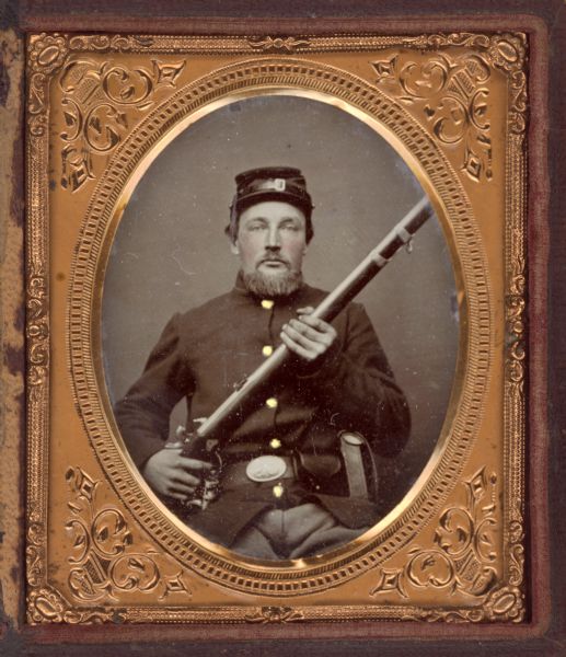 Sixth plate ferrotype/tintype of Simon O. Myhre of Company I, 15th Regiment, Wisconsin Infantry. Seated, facing forward, with rifle held up, pointing to upper right, his left hand on the trigger. He is wearing his uniform and cap, and full beard and mustache. Hand-coloring on cheeks and buttons. 