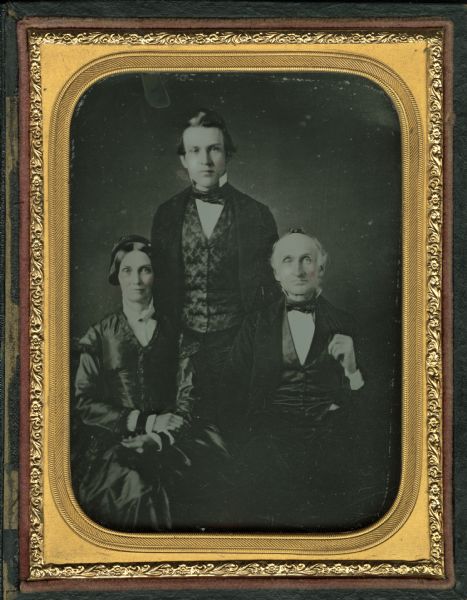 Quarter plate ambrotype. Group portrait of Leverett S. Kellogg and his wife are sitting, and their son is standing behind them in the center. Leverett and his son are wearing suits, vests and neck ties, and his wife is wearing a dark dress. Hand-coloring on cheeks.