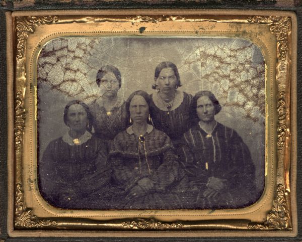 Quarter plate ferrotype/tintype of five Sawyer sisters, Sylvia, Zernia, Anna, Artemus, and Cordelia. They are facing front, and are wearing striped or printed dresses with white collars and brooches at the neck. They were daughters of Prescott Sawyer and pioneer women of Dane County in 1828. Gold details on jewelry. 