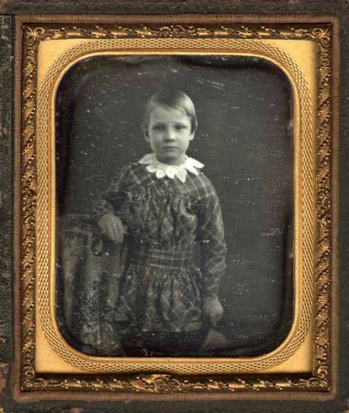Sixth plate daguerreotype of Henry S. Butler. Three-quarter length portrait, standing, facing forward. He is wearing a plaid shirt gathered and belted at the waist, with a white lace collar. His right forearm rests on a cloth covered table, his left hand at his side is possibly holding a cap. 