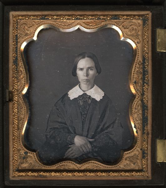 Quarter plate daguerreotype. Waist-up portrait of a woman posing with her hands in her lap. She is wearing a white lace collar and a beaded necklace over a dress with full length wide sleeves.
