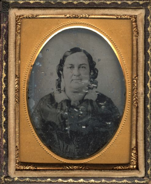 Ninth plate ambrotype of Emmeline S. Henshaw Whitney (Mrs. Daniel Whitney), from Green Bay, Wisconsin, originally from Middlebury, Vermont. Quarter-length portrait facing forward. She is wearing a dress of fine fabric, white lace collar and shoulder length side curls. 