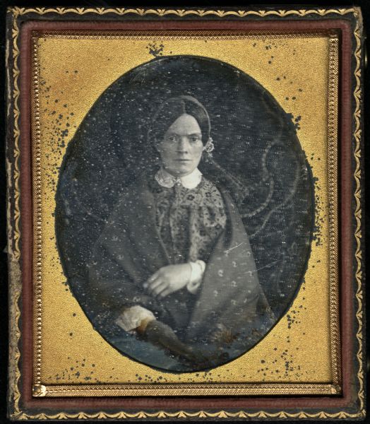 Sixth plate daguerreotype of three-quarter length portrait of unknown woman. She is seated, and is wearing a dress with a white collar, and a shawl over her shoulders.