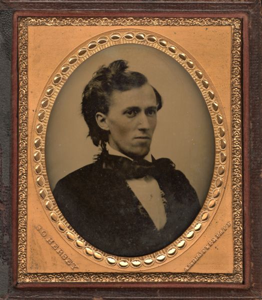 Sixth plate ambrotype of George Baxter Burrows. Quarter-length portrait, facing right. He is wearing a suit with printed vest and tie with fringed ends. He wears the top knot fashionable for men's hair in the early 1850s. Hand-coloring on cheeks.  