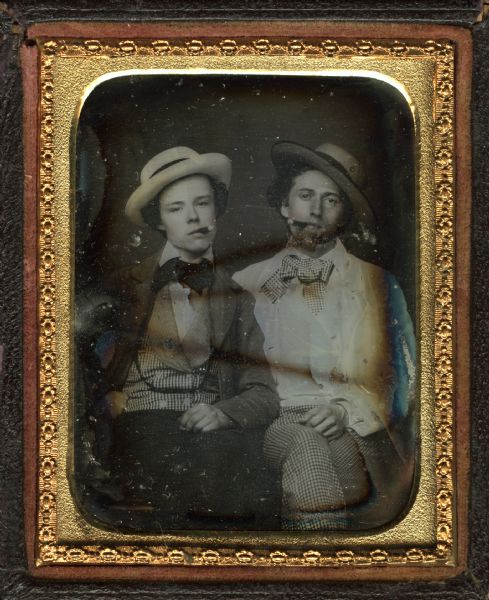 Ninth plate daguerreotype of George Baxter Burrows and his brother, seated with legs crossed, facing front, smoking cigars and wearing suits and straw hats typical of summer weather. George, on the right, wears checked pants and bow tie, while his brother's vest is of the same fabric. Hand-coloring on cheeks. 