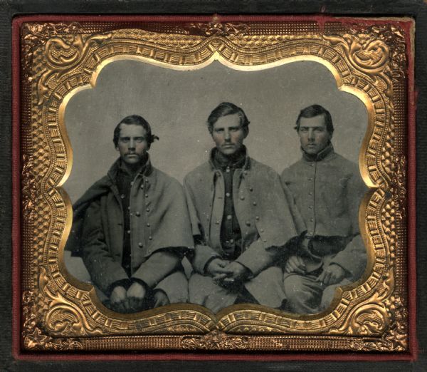 Sixth plate ferrotype/tintype of three unidentified soldiers, members of Company K, First Wisconsin Volunteers. They are seated facing forward with their hands in their laps, wearing their greatcoats over their uniforms. Hand-coloring on cheeks. 