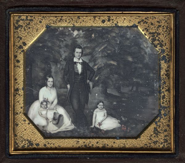 Sixth plate daguerreotype of a painting of a family with a woman on the left, a man standing in the center, and two young children. The backdrop is a pine forest. The father is wearing a suit and holding a hat in one hand and a walking stick in the other. The mother is seated at left, holding the arm of one daughter standing at her side, some flowers, and her bonnet. The other daughter is seated on the ground on the right. The mother and her daughters are wearing white dresses and are holding pink flowers. 