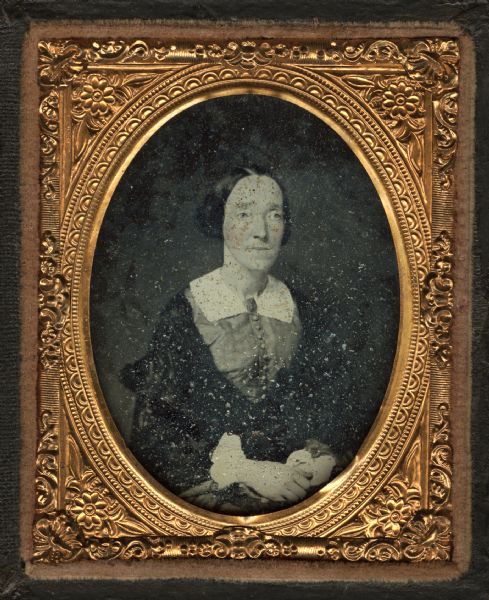Ninth plate ambrotype of Anne Marie Alcott Lapham (Mrs. Increase A. Lapham). Waist-up portrait, facing slightly right, hands folded in lap, wearing a dress buttoned down the front, white collar and brooch, and shawl. Hand-coloring on cheeks. 