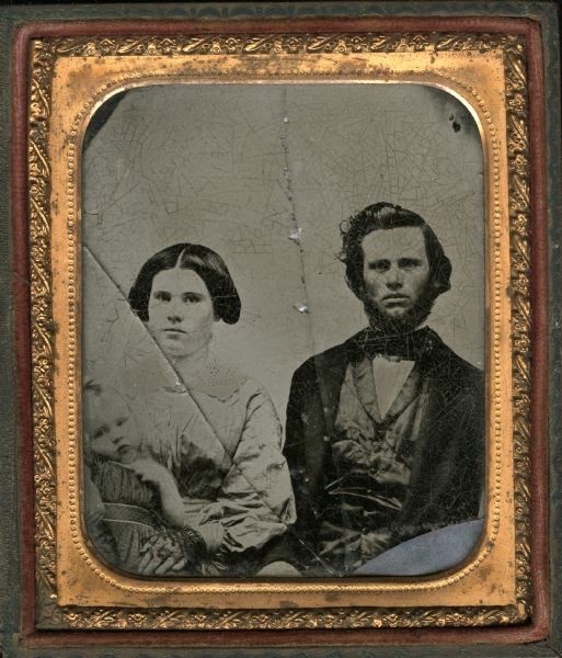 Sixth plate ambrotype of Ansom, Mary, and Leroy Case. Waist-up portrait, seated, facing forward. Mary is wearing lace fingerless gloves, and a dress with gathered bodice and cutwork collar, and is holding Leroy on her lap. Ansom is wearing a suit with a satin vest. Ansom and Mary were the parents of Belle Case, and Leroy was her brother. 