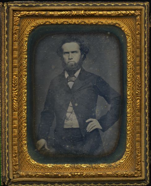 Quarter plate daguerreotype of Captain Nathaniel Rollins (1832-1901). Half length portrait, standing, facing forward with left hand on hip and right resting on a table. He wears a suit coat with only the top button closed, and his pocket watch key & chain visible on his buttoned vest. 