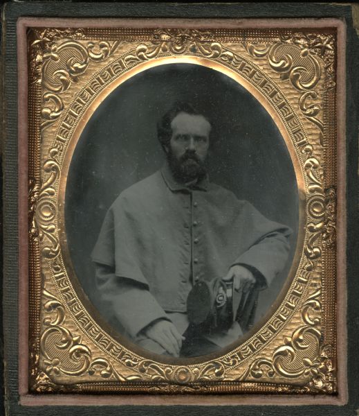 Sixth plate ferrotype/tintype of Captain Nathaniel Rollins (1832-1901). Waist-up portrait, seated, facing forward. He is wearing his Civil War greatcoat. He is sitting sideways in a chair, and has his elbow resting on the back of it, and he is holding his uniform cap in his hand.