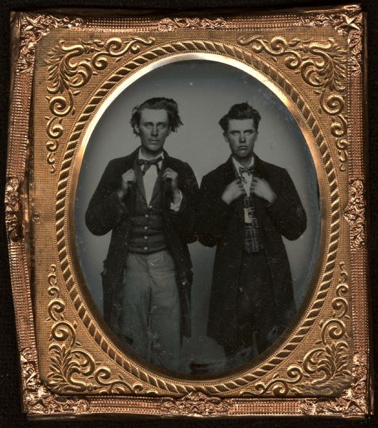 Sixth plate ambrotype. Three-quarter length portrait of George Searles and George Olmstead (r.), standing, facing forward, with their hands holding their lapels. Each man is wearing a long coat, vest (Olmstead's is plaid), and small bow tie. 