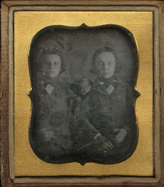 Sixth plate daguerreotype. Waist-up portrait of Edward S. and Hollis C. Wade, sitting in chairs, facing forward, wearing buttoned suit coats, cravats, and stand collars. Their hair is ear length. The child on the left rests his left arm on the shoulder of the other boy. 