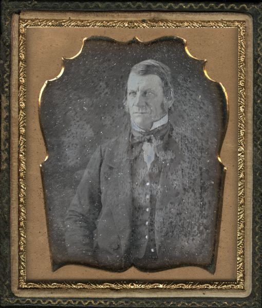 Sixth plate daguerreotype of unidentified man. Waist-up portrait, facing slightly left, wearing suit, cravat, and stand collar. Sideburns extend below his ears.  