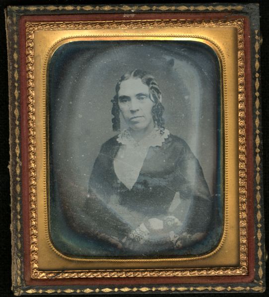 Sixth plate daguerreotype of Mrs. James Campbell Hopkins. Waist-up portrait, facing front, torso facing slightly left, with an inward gaze. She is wearing a dark, habit front dress with white lace collar, cuffs, and mitts. Her hair is done in ringlets in front of the ears. 