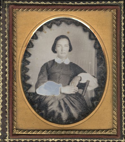 Sixth plate daguerreotype of Jeanette Haseltine Decker Sheldon. Three-quarter length portrait, facing forward, sitting sideways on a chair with her forearm resting on the chair back, hands clasped. She is wearing a dark fan front dress with white collar and chemise sleeves, black cuffs.  